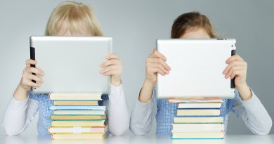 Two pupils leaning on a pile of books while reading on touchpad