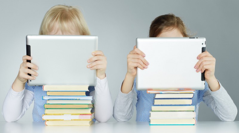 Two pupils leaning on a pile of books while reading on touchpad